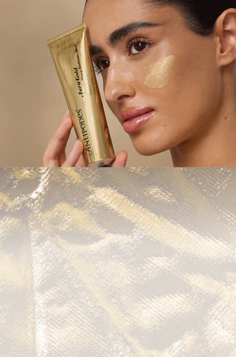 Woman applying gold-colored cosmetic product to her face with a textured beige background