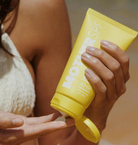 Person holding a yellow sunscreen bottle with 'MOTHER' branding.