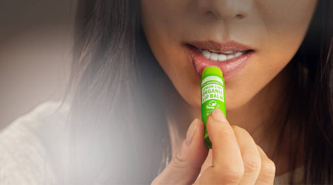 Person holding a Dr Bronner's lemon lime lip balm close to their mouth