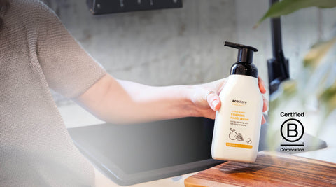 Person holding a bottle of handwash with a sink and plant in the background