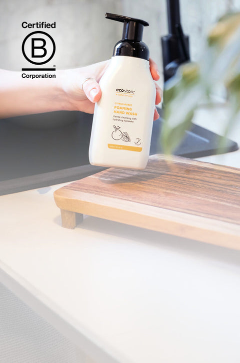 Person holding a bottle of handwash with a sink and plant in the background