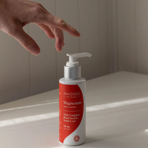 Hand reaching towards a bottle of Amazing You magnesium joint lotion on a light surface.