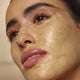 Close-up of a woman's face with aura gold facial mask applied to her cheek.