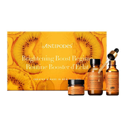 Antipodes Brightening Boost Regime skincare product set with bottles & packaging featuring kiwi fruit on a white background.