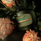 Bottle of Antipodes Peach Freesia conditioner surrounded by flowers on a dark background.