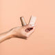 Hand holding a bronzer stick & packaging against a beige background