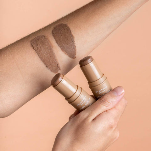 Two swatches of bronzer stick on a person's forearm, showing both stick shades next to it.