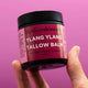 Jar of Ylang Ylang Tallow Balm held by a hand against a pink background