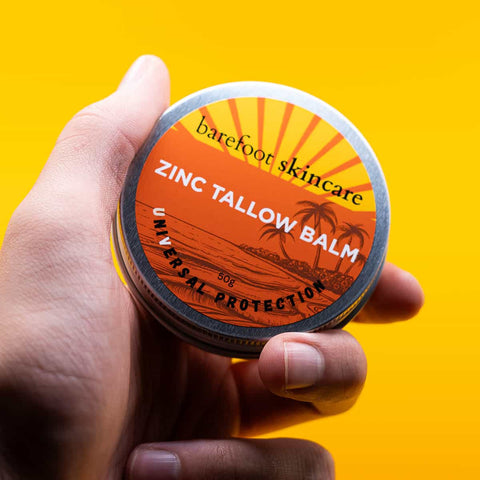 Hand holding a container of barefoot skincare zinc tallow balm against a yellow background