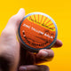 Hand holding a container of barefoot skincare zinc tallow balm against a yellow background