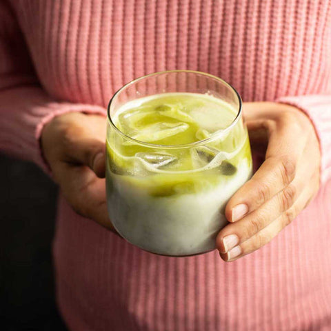 Person holding a glass of iced matcha latte with a pink sweater