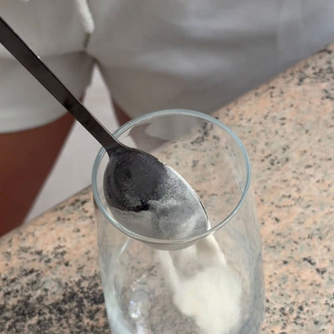 Spoon with collagen powder over a glass on a speckled countertop.
