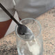 Spoon with collagen powder over a glass on a speckled countertop.