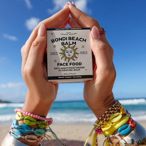 Person holding a 'Bondi Beach Balm' product with a beach in the background