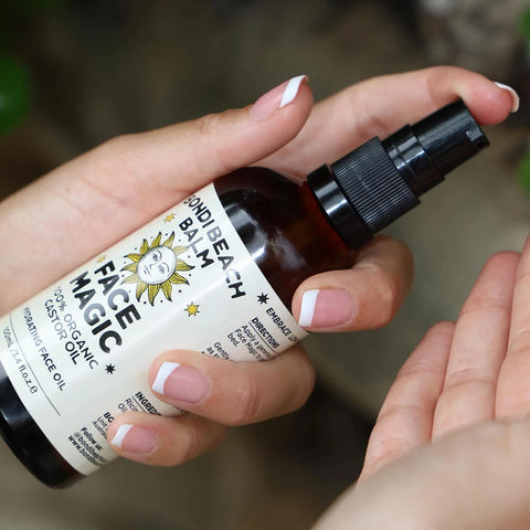 Hand holding a bottle of 'Face Magic' organic castor oil face oil with a spray nozzle.