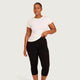 A woman modeling a white short-sleeve crewneck t-shirt and black high-waisted capri leggings against a light gray studio background.