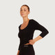 A woman modeling a black three-quarter sleeve scoop-neck athletic top and matching black leggings against a light gray studio background. The brand name 'boody' is visible on the waistband of the leggings.
