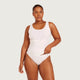 A plus-size model wearing a white ribbed tankini swimsuit against a light gray studio background.