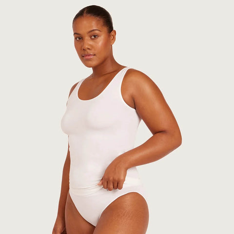 A woman modeling a white sleeveless bodysuit or one-piece swimsuit against a light gray studio background.