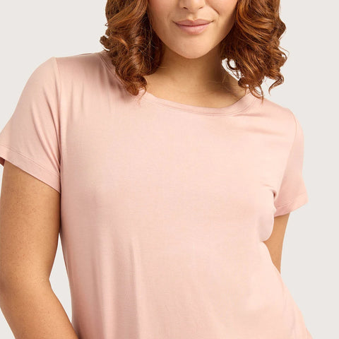 A close-up of a woman wearing a light pink short-sleeve crewneck t-shirt against a solid light gray background.