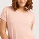 A close-up of a woman wearing a light pink short-sleeve crewneck t-shirt against a solid light gray background.