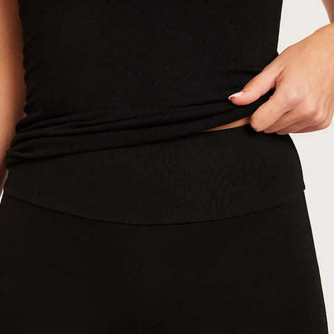 Close-up of a person wearing black leggings and lifting the hem of a black top to show a built-in waistband detail.