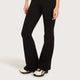 Black flared pants worn by a model, paired with cream and black sneakers, shown from the waist down against a light gray studio background.