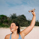 Woman on a beach holding a collagen bar above her head