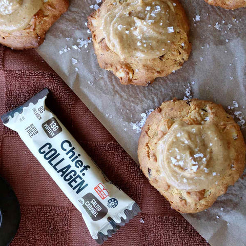 Cookies with a salted caramel topping on brown baking paper, next to a package of Chief Collagen salted caramel protein bar.