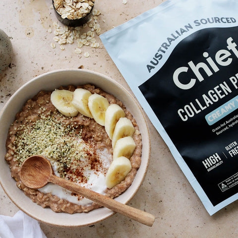 Bowl of oatmeal with bananas and a package of Chief Collagen Powder on a beige surface.