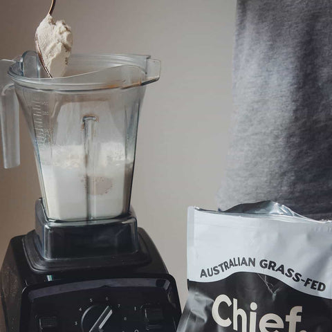 Blender with milk and whey powder being scooped into it for mixing into a smoothie.