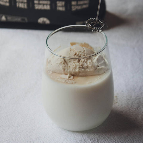 Glass of milk with a scoop of vanilla whey protein powder with a supplement whisk used for blending.