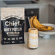 Chief whey protein package with a glass of a protein smoothie on a kitchen counter with bananas in a fruit bowl.