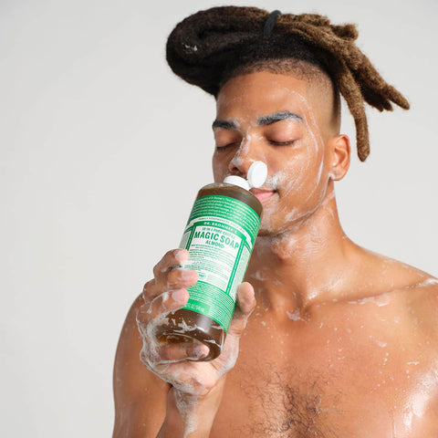 Man applying Dr. Bronner's Magic Soap to his face against a plain background.