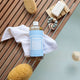 Bottle of Dr. Bronner's 18-in-1 Pure-Castile Magic Soap with a white towel on a wooden surface with bath accessories.