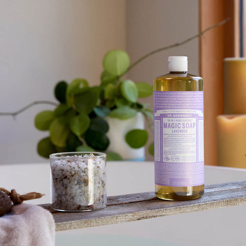 Bottle of Dr. Bronner's 18-in-1 Pure-Castile Magic Soap - Lavendar on a surface with a candle & plant in the background.