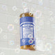 Bottle of Dr. Bronner's 18-in-1 Pure-Castile Magic Soap - Peppermint on a tiled bathroom wall with bubbles.