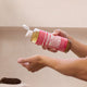 Hand holding a bottle of Dr. Bronner's 18-in-1 Pure-Castile Magic Soap - Rose over another hand.
