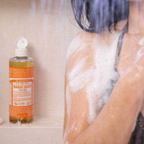 Bottle of Dr. Bronner's Magic Soap Tea Tree on a bathtub ledge with a person showering in the background.
