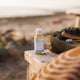 Bottle of Dr. Bronner's Pure-Castile Soap on a wooden surface with a beach background.
