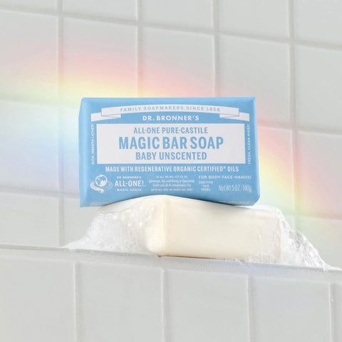 Dr. Bronner's Magic Bar Soap Baby Unscented in a bathtub with a rainbow & tiled wall background.