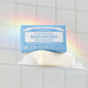 Dr. Bronner's Magic Bar Soap Baby Unscented in a bathtub with a rainbow & tiled wall background.