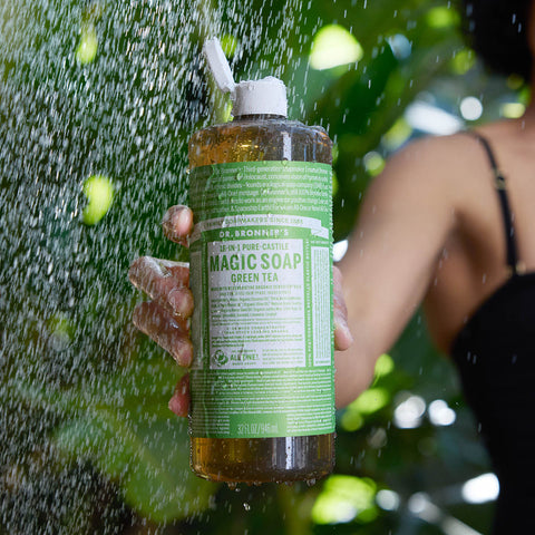 Person holding a bottle of Dr. Bronner's Magic Soap Green Tea under running water.