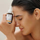 A small amber dropper bottle labeled Dr. Hauschka Hydrating Serum Plus stands beside a lemon and a long root on a clean light gray studio background.