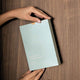 Hand holding baby laundry detergent sheets against a wooden surface. Light blue cardboard packaging with 80 fragrance free sheets. 