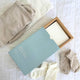 Baby clothes and items including a shirt, socks, and baby laundry detergent sheets on white bedding.