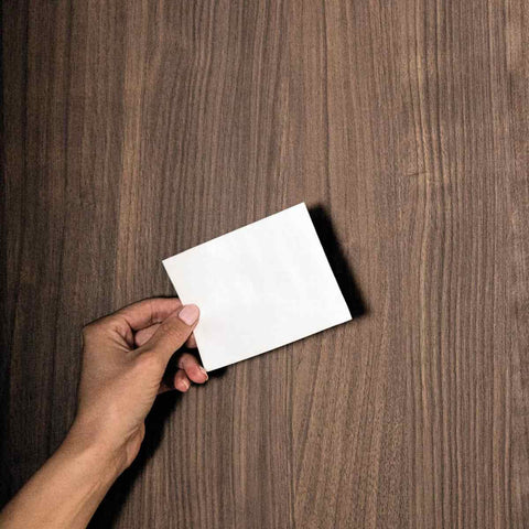 Hand holding a single shite detergent sheet against a wooden background.