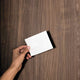 Hand holding a single shite detergent sheet against a wooden background.