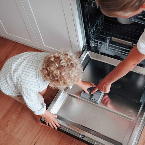 Mother and child putting dishwasher detergent sheets into dispenser of dishwasher.