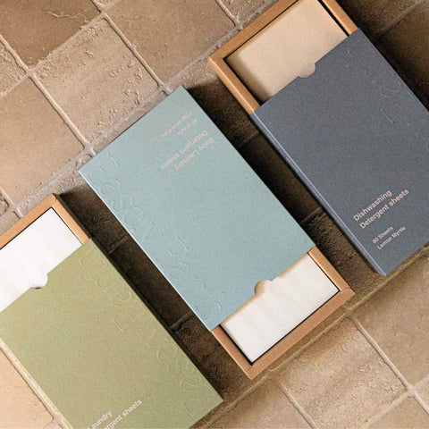 Three packages of Ease.y Earth laundry & dishwashing detergent sheets on a tiled floor.